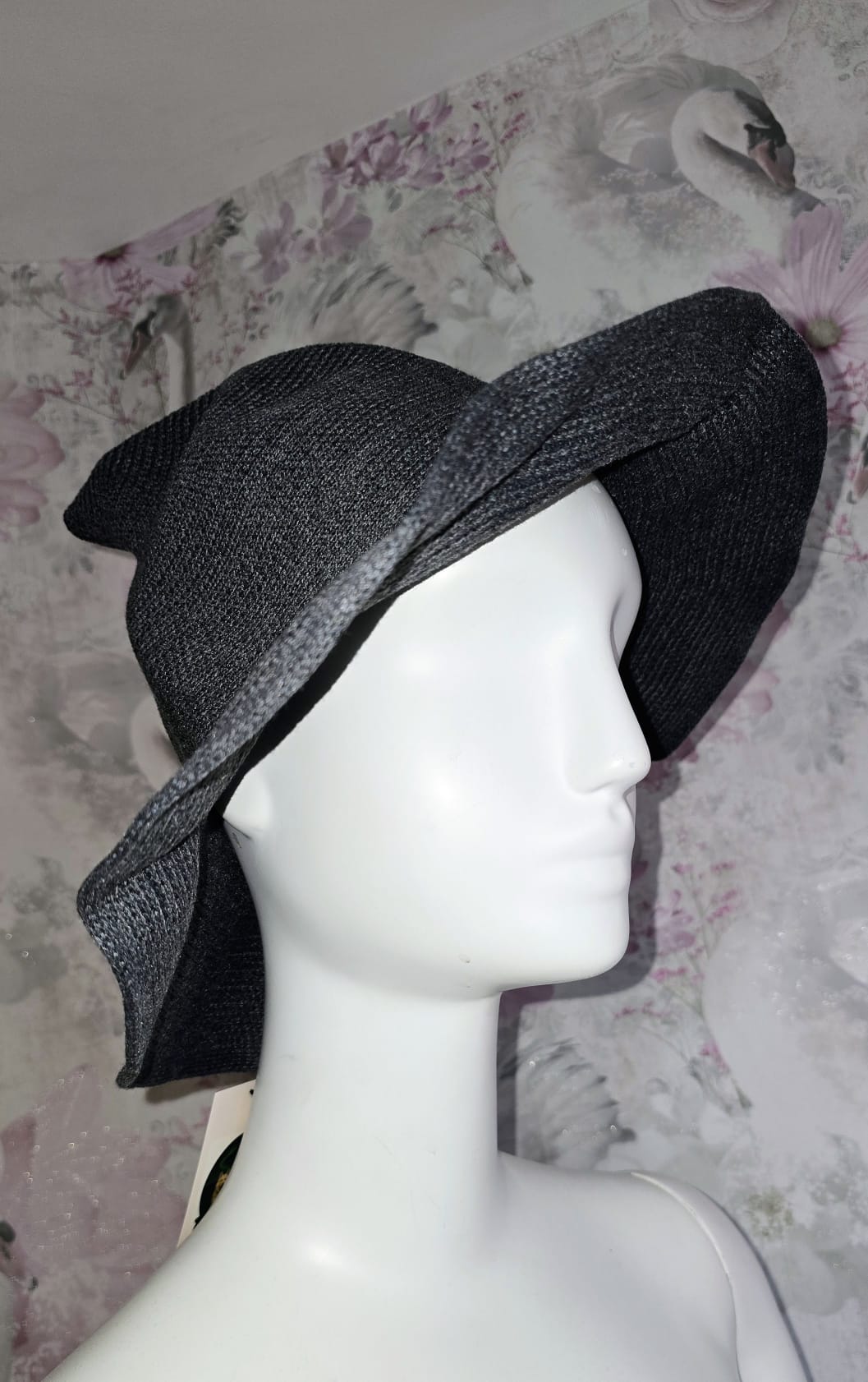 Black straw hat on a mannequin head against a floral wallpaper background