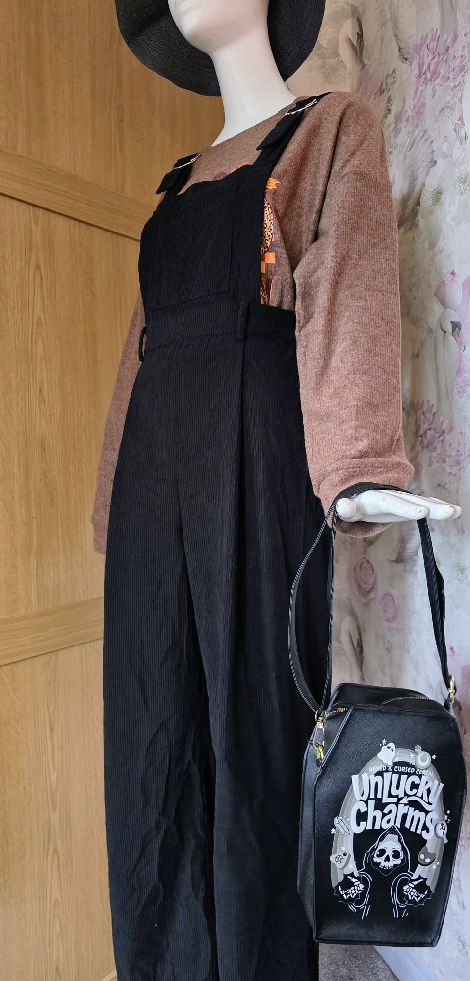 Mannequin wearing a black outfit with a pink sweater and black bag featuring white text.