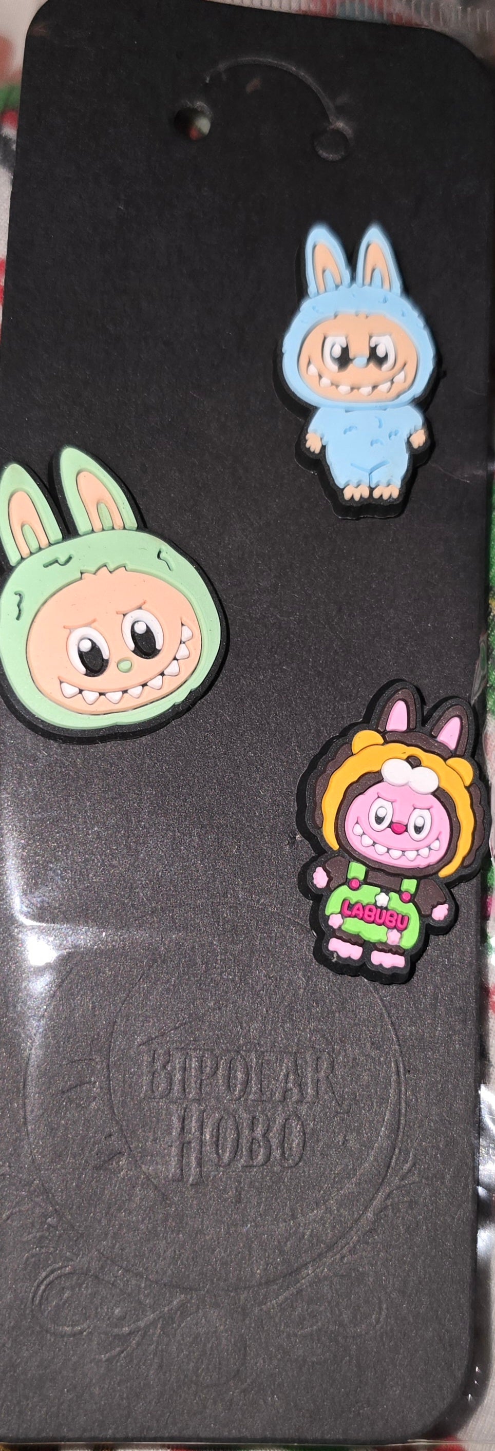 Three cartoon character pins on a black card with 'Kipling' branding.
