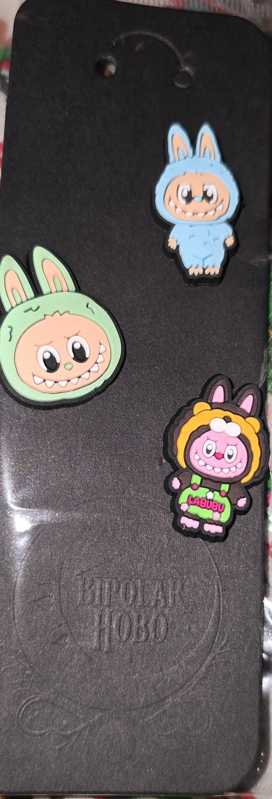 Three cartoon character pins on a black card with 'Kipling' branding.