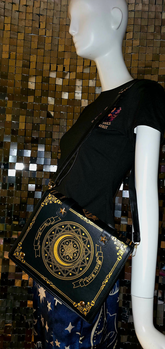 Mannequin wearing a black dress with a decorative gold and black bag against a mosaic wall.