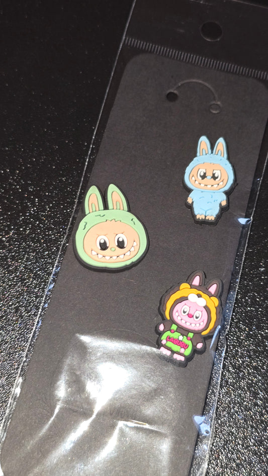 Three colorful cartoon character pins on a black surface