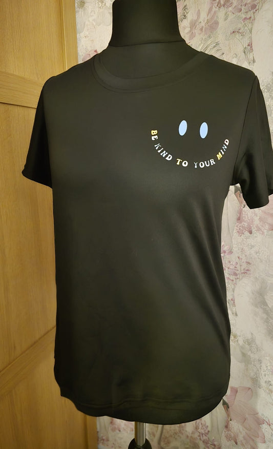 Black t-shirt with a smiley face design on a mannequin against a floral wall.