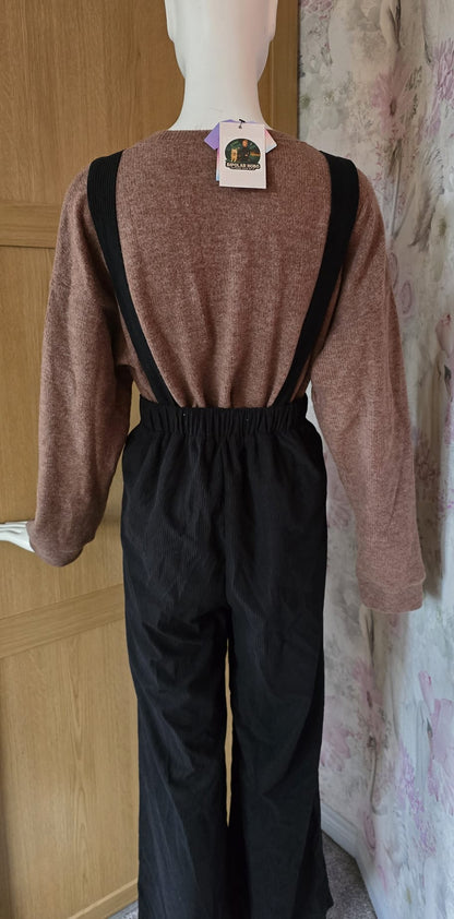 Mannequin wearing a brown sweater and black overalls with a tag, against a wooden door and floral wall.